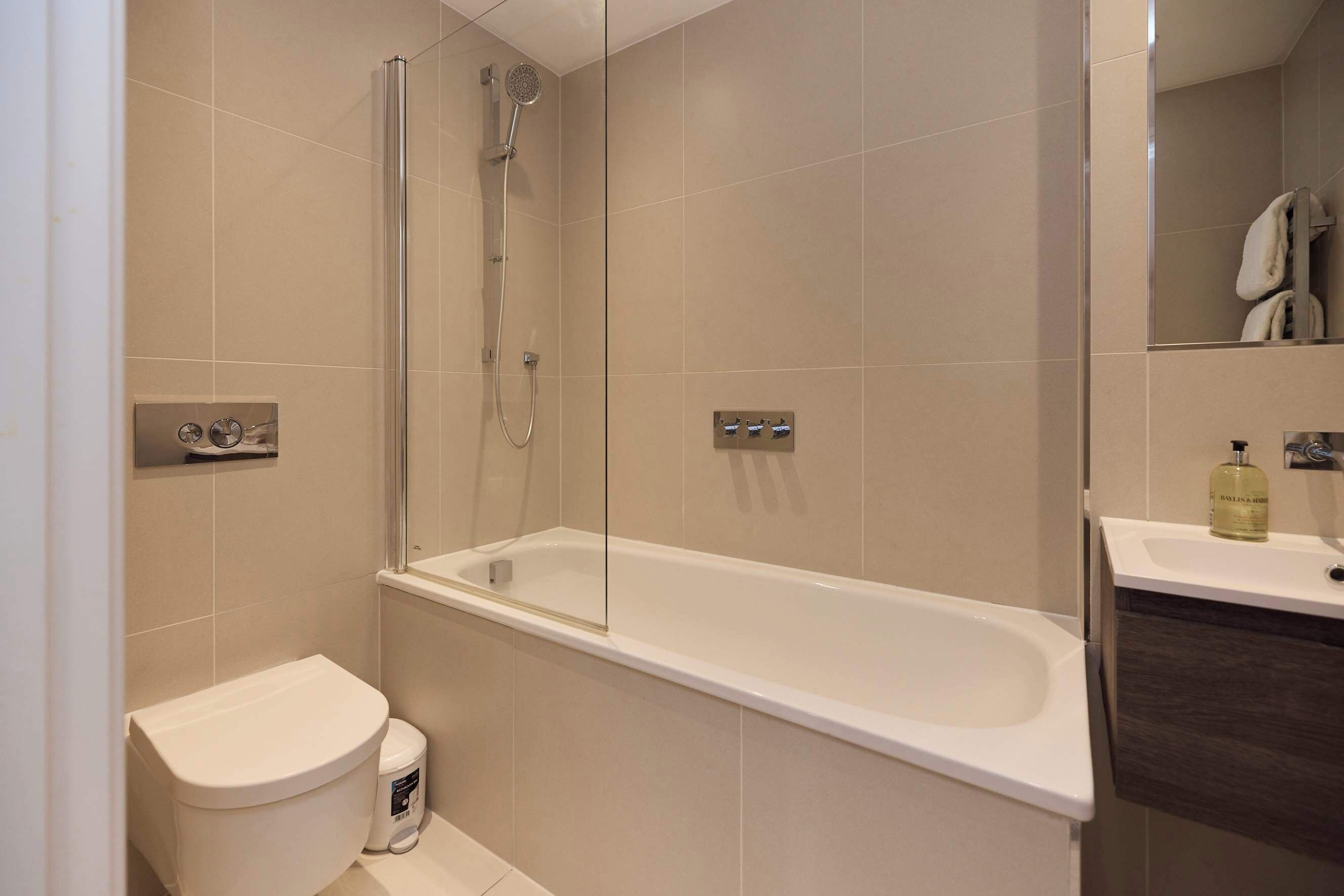 A modern bathroom with a glass-enclosed shower, a white bathtub, and a toilet.