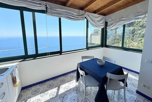 Ein Zimmer mit Meerblick, einem Tisch mit Stühlen und einem Fenster mit Vorhängen.
