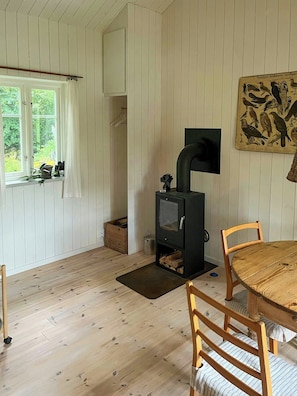 Ett mysigt rum med trägolv, ett bord med stolar, en öppen spis, ett fönster med gardiner och en väggmonterad tv.