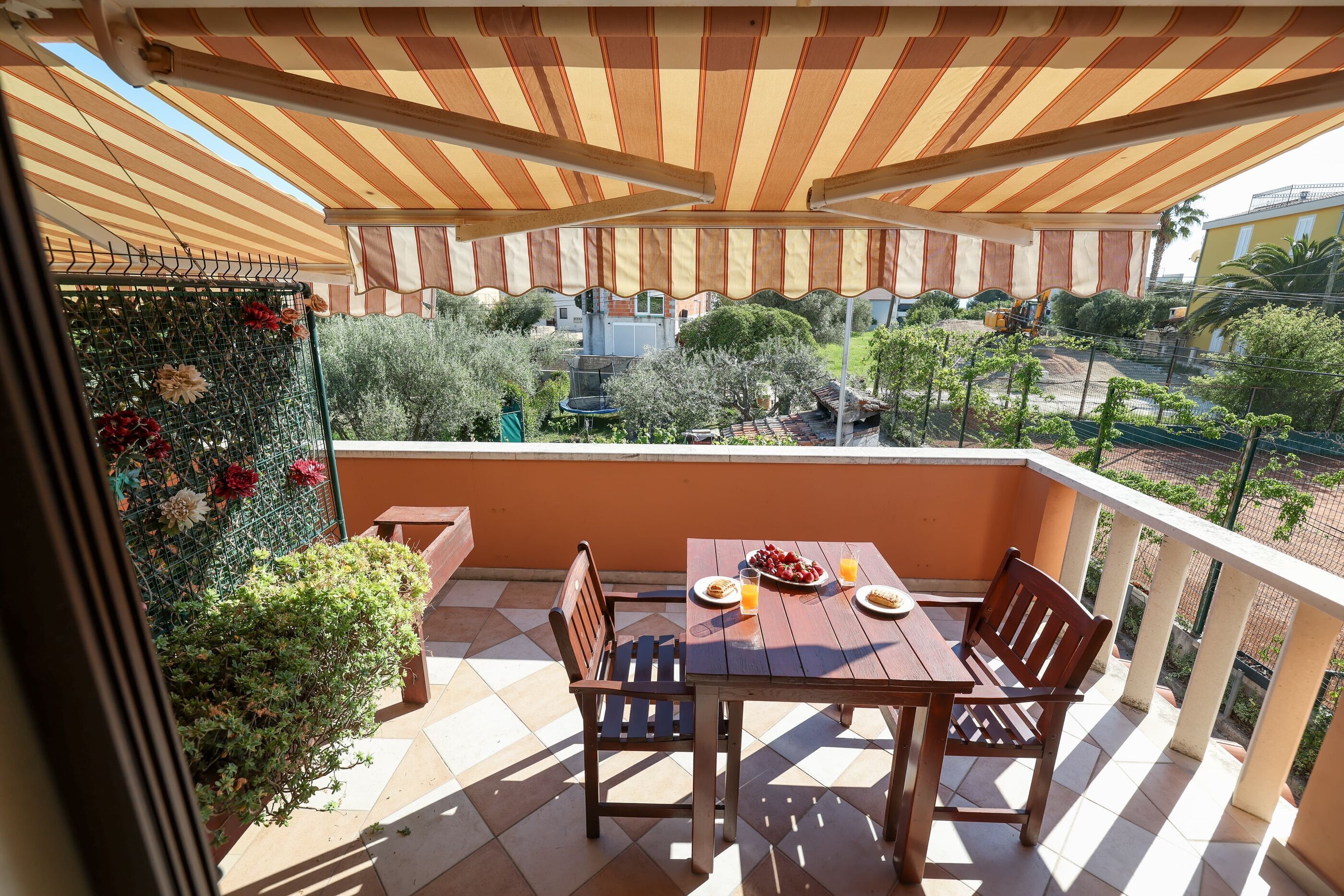 A balcony with a striped awning, a table with chairs, and a view of the surrounding area.