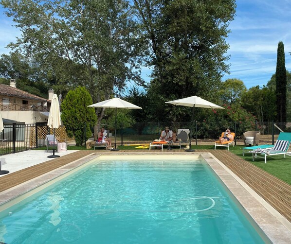 Una piscina amb gandules i ombrel·les, envoltada de vegetació i una zona tancada per una tanca.