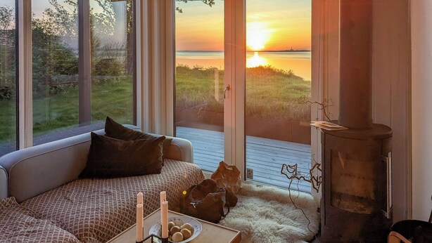 A cozy room with a sofa, a fireplace, and a view of a sunset over water.