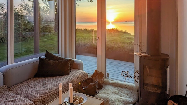 A cozy room with a sofa, a fireplace, and a view of a sunset over water.