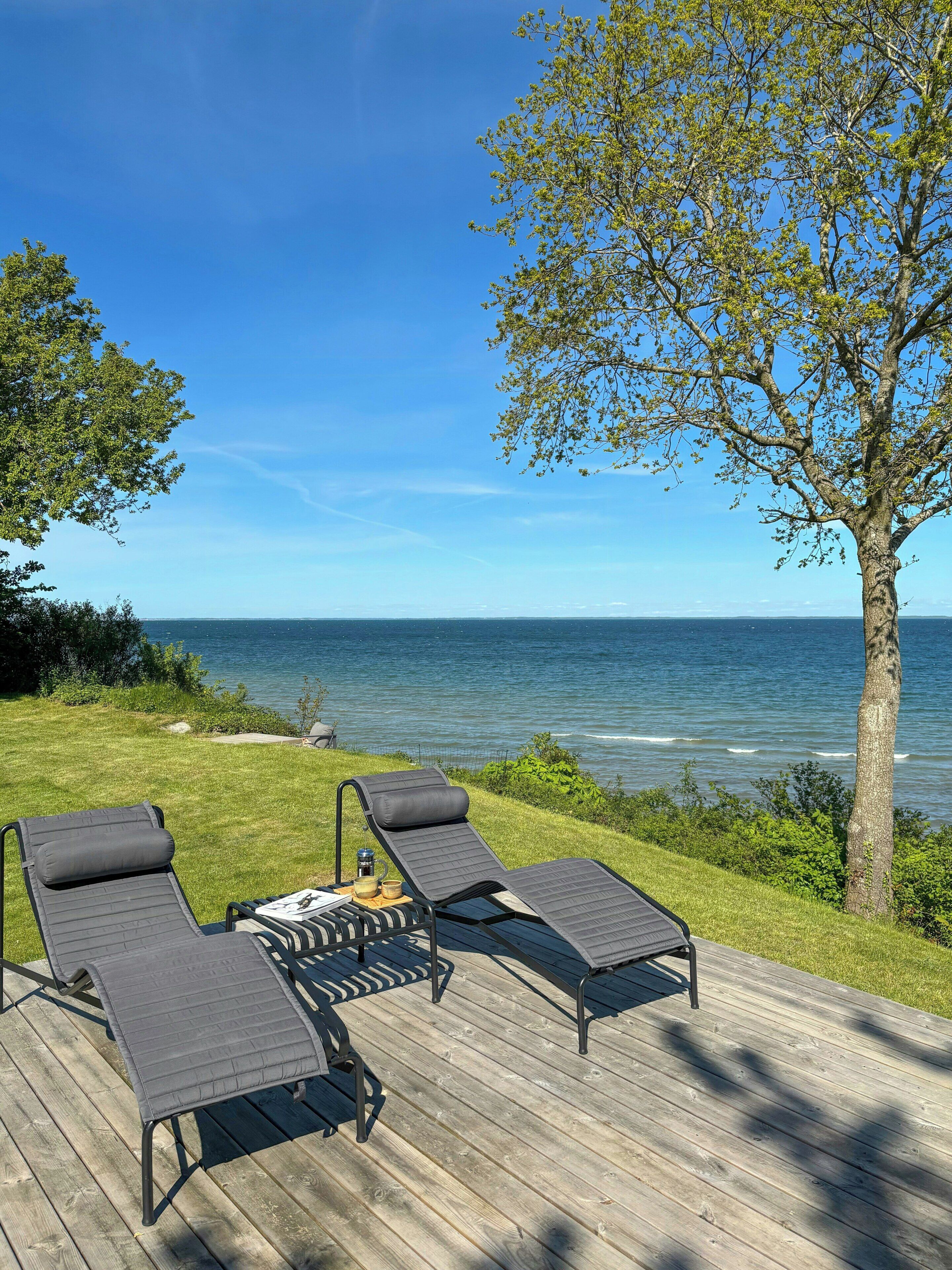 En terrasse med to liggestole og et bord, med udsigt over vandet.