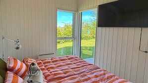 A bedroom with a bed, a desk, a lamp, and a window with a view of greenery.