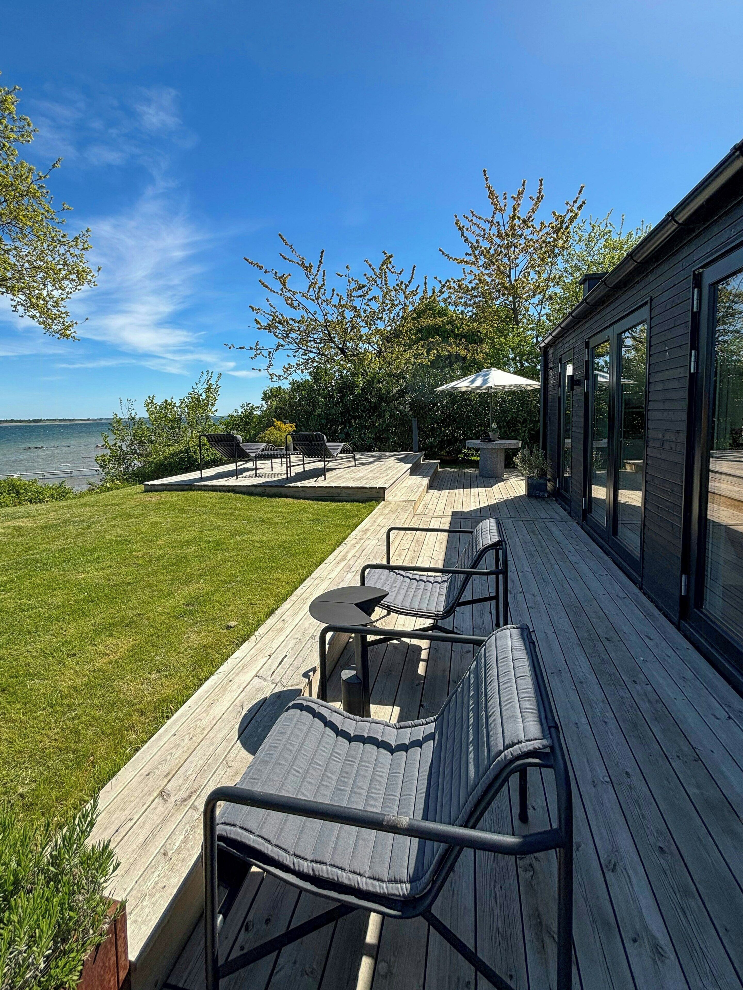 Una terraza con mobiliario exterior, vista al agua y un edificio con ventanas amplias.