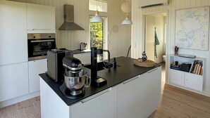 A modern kitchen with white cabinetry, a large island, a coffee machine, and pendant lights.