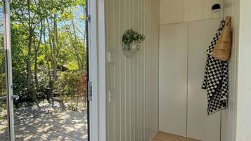 A wooden deck leading to a room with a sliding door, a small shelf with plants, a checkered towel, and a woven bag.