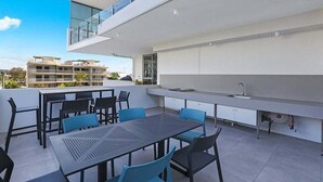 Et moderne udendørs spiseområde med bord og stole, en indbygget vask og udsigt over byen.
