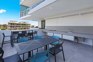 Ein moderner Essbereich im Freien mit Tisch und Stühlen, einer integrierten Spüle und Blick auf die Stadt.