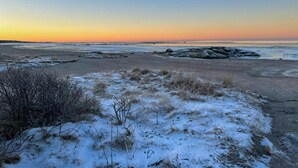 En strand med snötäckt sand, en klar himmel och avlägsna klippformationer.