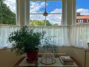 Ein Zimmer mit großem Fenster, einem Blumentopf, einem Tisch mit Büchern und einer Pendelleuchte.