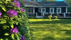 A house with a porch, a fenced yard, and a tree with purple flowers. - Summer house by protected heathland in Ellinge (Højby)