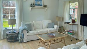 A living room with a white sofa, a coffee table, a lamp, a TV, and a bookshelf. - Summer house by protected heathland in Ellinge (Højby)