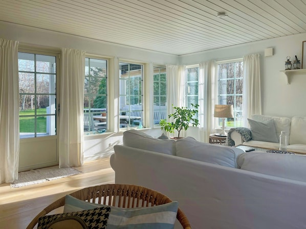 A spacious room with a large bed, a sofa, a dining table, and multiple windows offering a view of the outdoors. - Summer house by protected heathland in Ellinge (Højby)