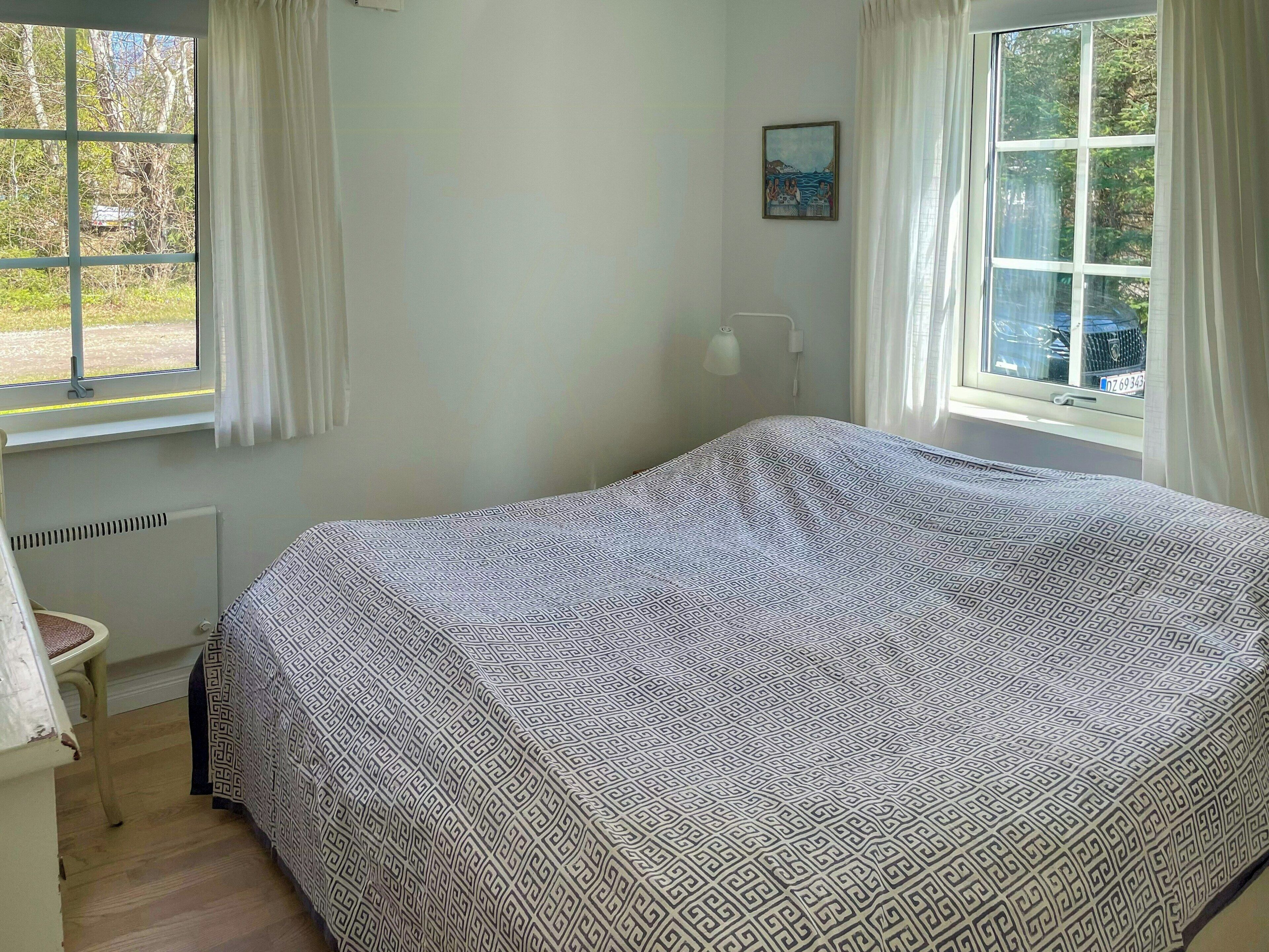 Quarto com cama, radiador, cadeira e janela com cortinas.