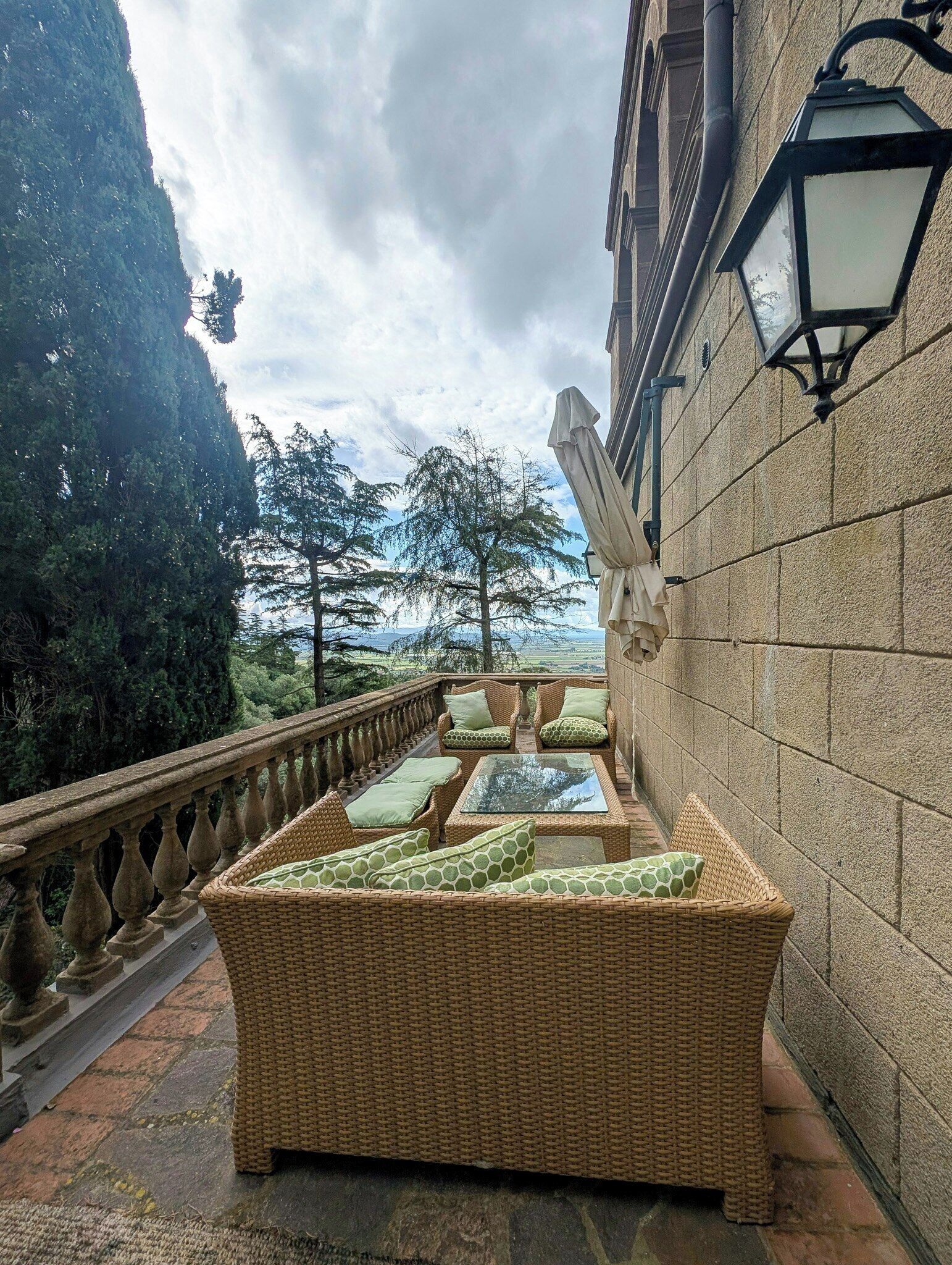 Un balcon agrémenté de meubles en osier, d’une balustrade en pierre et offrant une vue sur le paysage.