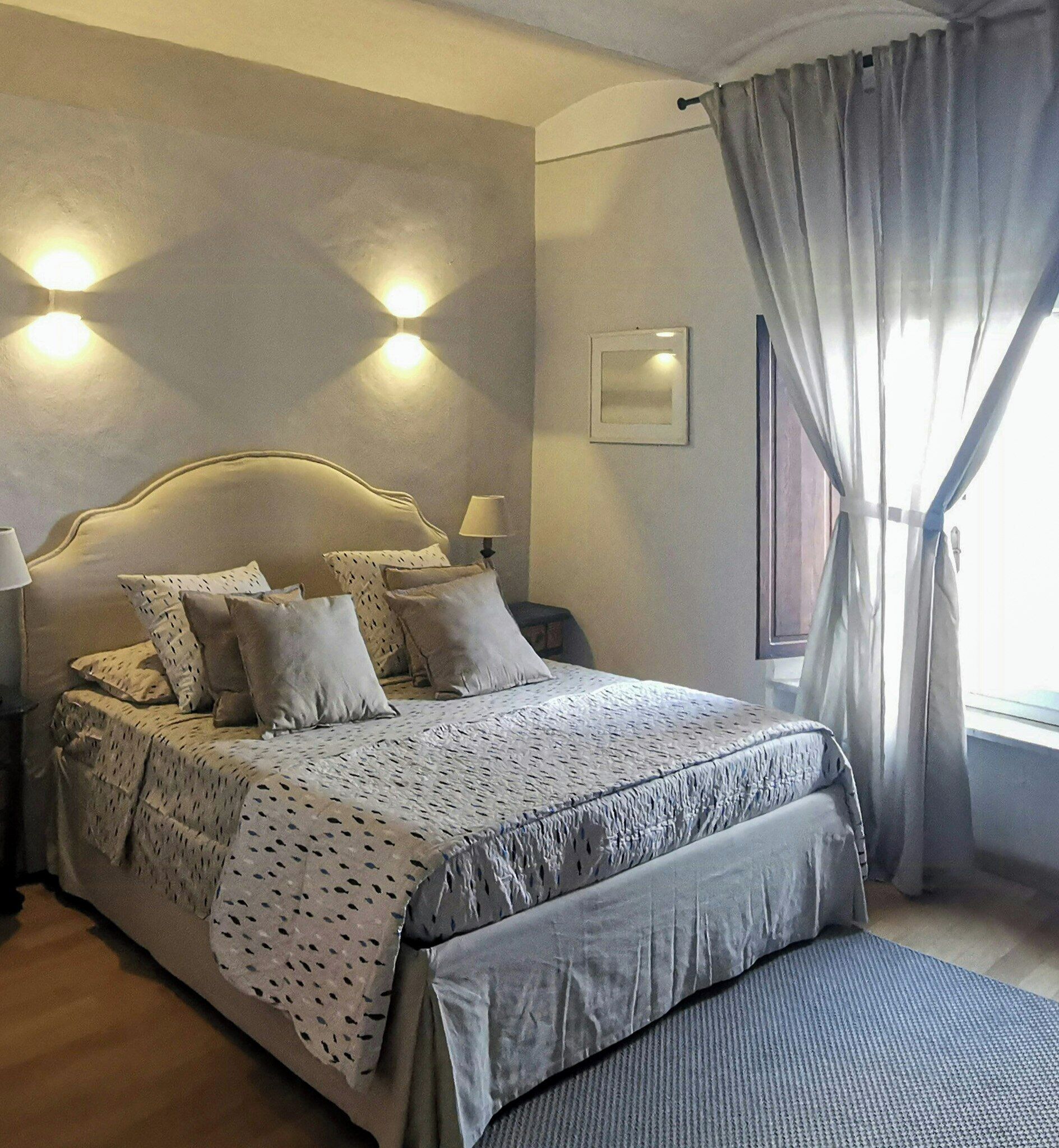 A neatly made bed with a patterned bedspread, a bedside table with a lamp, and a wall-mounted light fixture.