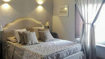 A neatly made bed with a patterned bedspread, a bedside table with a lamp, and a wall-mounted light fixture.