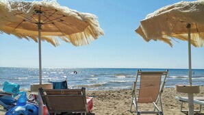 A beach with two umbrellas, lounge chairs, and a shark float. - Small castle with sea view in Campiglia Marittima (Campiglia Marittima)