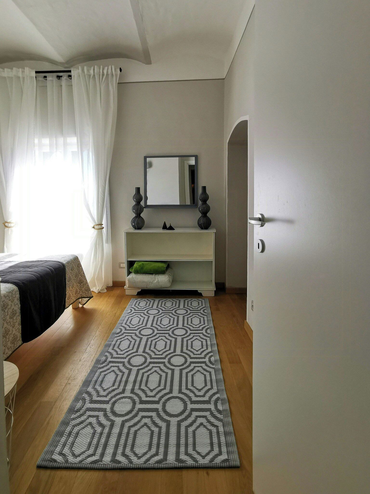 A bedroom with a bed, a bedside table, a mirror, a dresser, and a patterned rug.