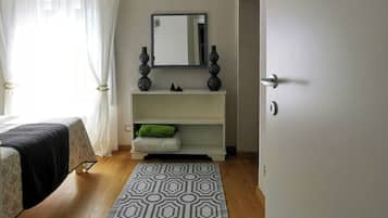 A bedroom with a bed, a bedside table, a mirror, a dresser, and a patterned rug.