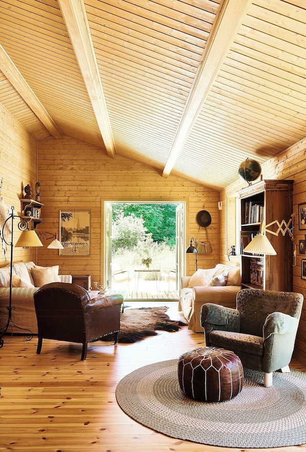 Ein Holzinnenraum mit Sofa, Sesseln, Hocker, Bücherregal und einer Lampe.