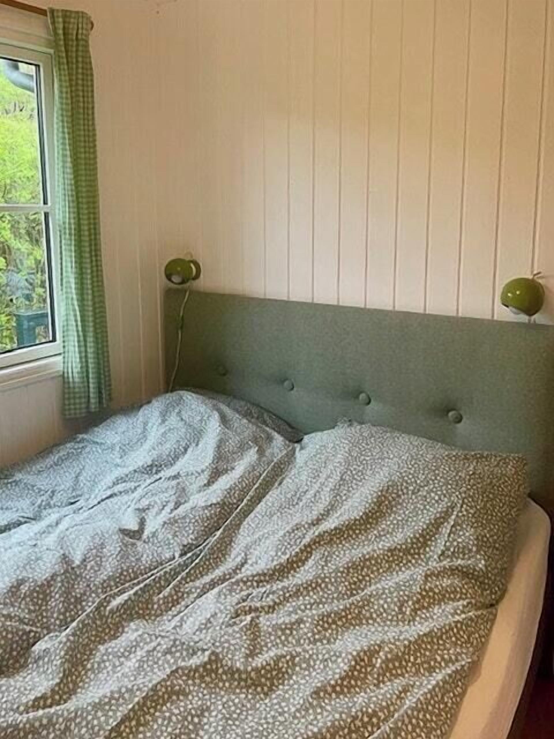 Un lit avec une couvre-lit à motifs, une tête de lit verte et une fenêtre avec un rideau vert.