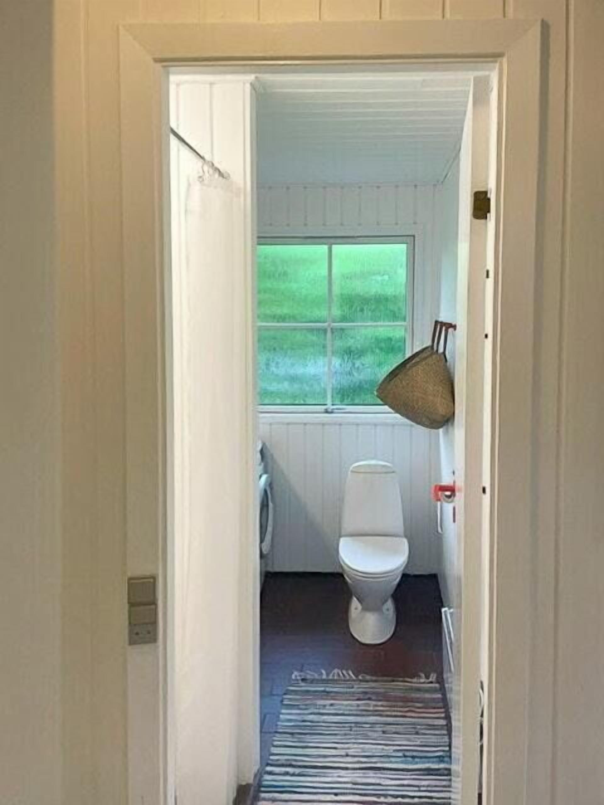 A narrow hallway leading to a small bathroom with a toilet, a window, and a hanging basket.