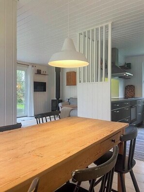 Een eetgedeelte met een houten tafel en stoelen, een hanglamp en uitzicht op de keuken.