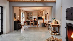 A cozy living room with a fireplace, wooden beams, a bookshelf, and a dining area. - Light-filled natural retreat near the Baltic Sea (Kalkhorst)