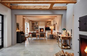 A cozy living room with a fireplace, wooden beams, a bookshelf, and a dining area. - Light-filled natural retreat near the Baltic Sea (Kalkhorst)