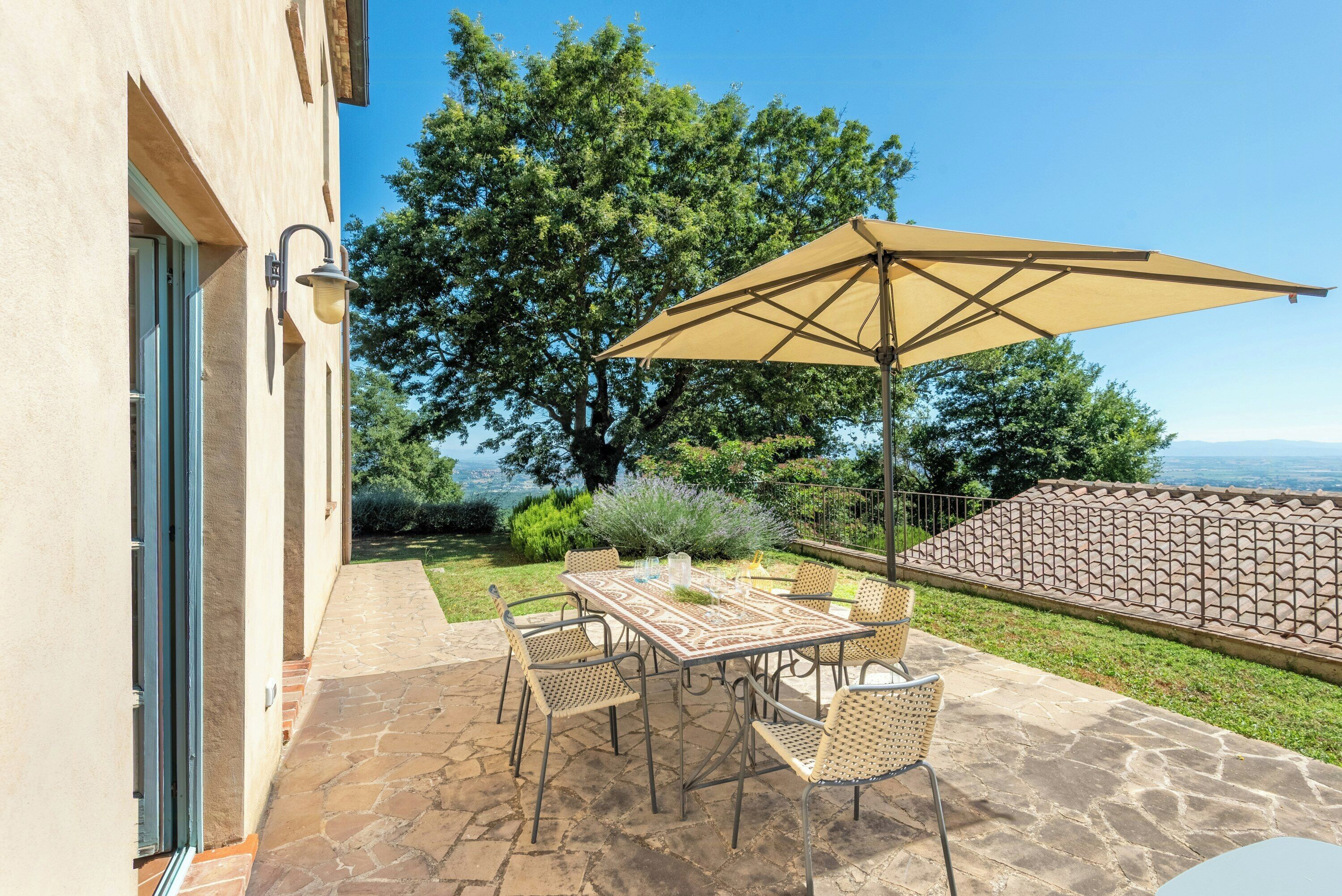 Une terrasse extérieure avec une table et des chaises, un grand parasol et une vue sur le paysage.