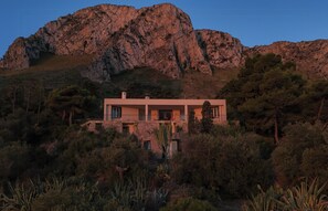 Ein modernes Haus mit Flachdach, umgeben von dichter Vegetation und einem Berg im Hintergrund.