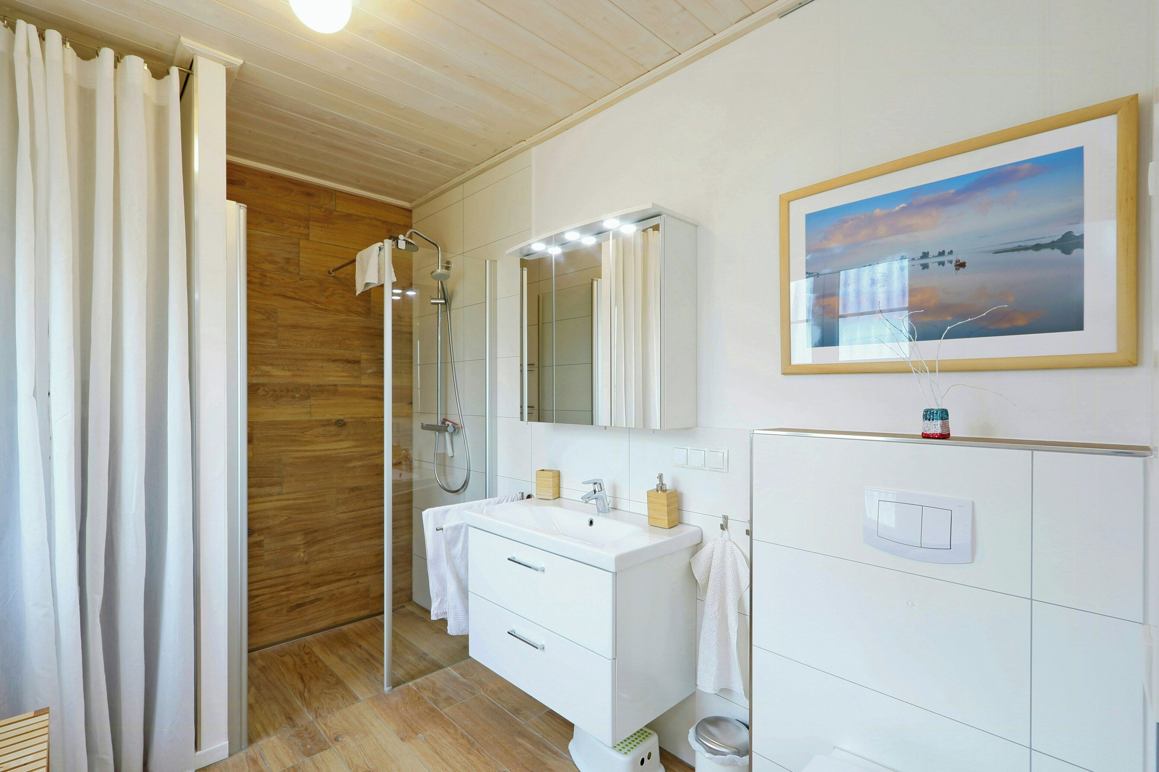 A bathroom with a wooden shower, a white sink with a mirror, and a framed picture on the wall.