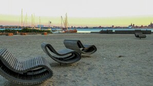 En strand med solstolar och utsikt över vattnet och stadsbilden i fjärran.