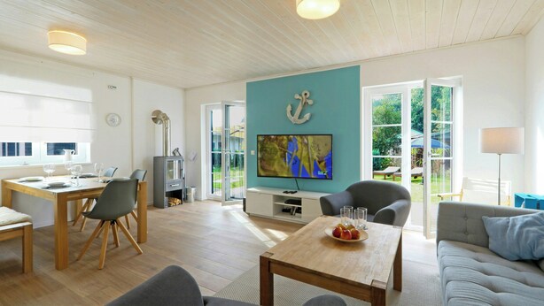 Ett rymligt vardagsrum med ett träpanelat tak, ett matbord, en soffa och en tv som är monterad på en turkosfärgad vägg.