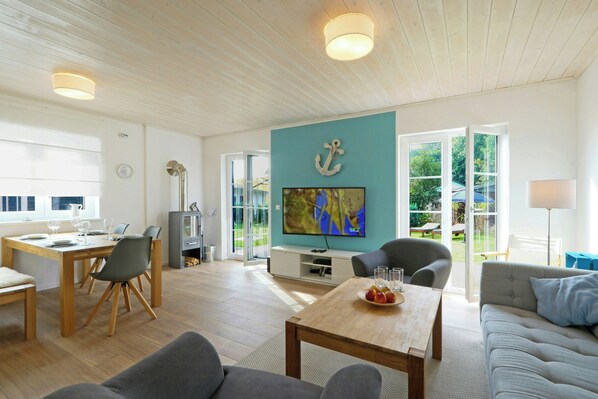 A spacious living area with a wooden ceiling, a dining table, a sofa, and a TV mounted on a teal wall. - Family home near beach in Altefähr on Rügen (Altefähr)