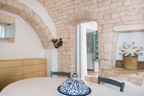 A dining area with a white table, chairs, and a decorative blue and white ceramic piece. - Historic trullo in Valle d'Itria (Ostuni)