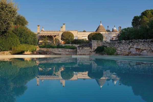 A pool reflecting a stone building with arched windows and a dome. - Historic trullo in Valle d'Itria (Ostuni)