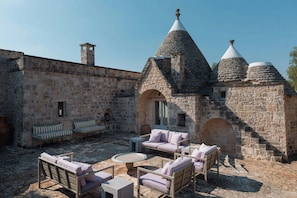 A courtyard with stone walls, a stone building with conical roofs, and outdoor furniture. - Historic trullo in Valle d'Itria (Ostuni)