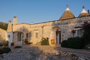 A stone building with a courtyard, arched doorways, and a large vase. - Historic trullo in Valle d'Itria (Ostuni)