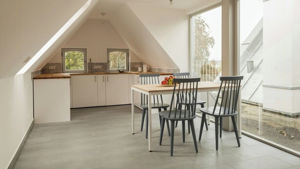 A modern kitchen with white cabinets, a wooden countertop, and a dining area with a table and chairs. - Wide view on nature from the manor house on Rügen (Poseritz)