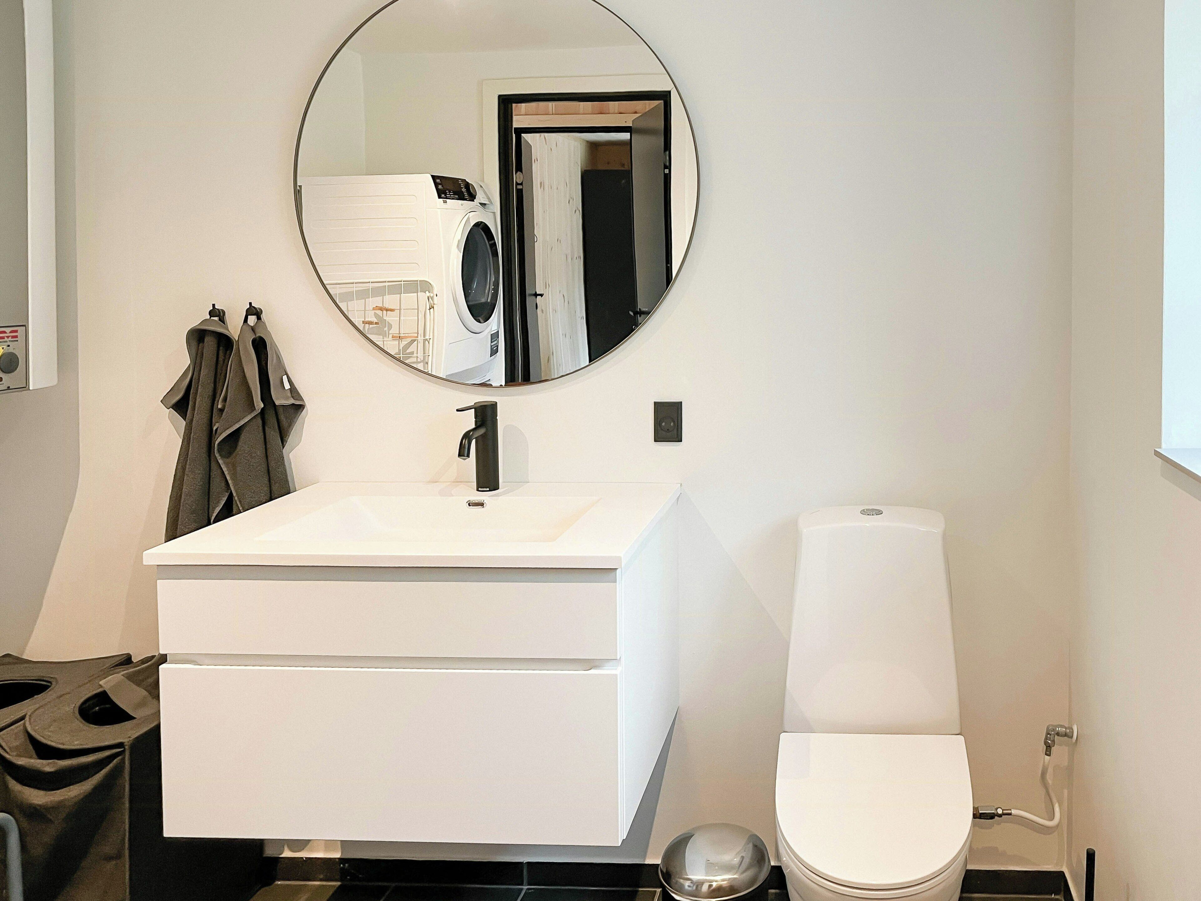Un bagno moderno con un lavandino bianco, uno specchio rotondo, un water e un porta asciugamani.