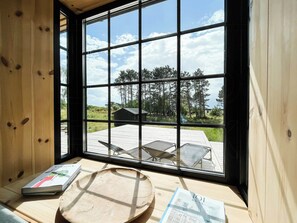 A room with a large window, wooden walls, a wooden table, and a book. - Serenety with a sea view amidst preserved nature (Kalundborg)