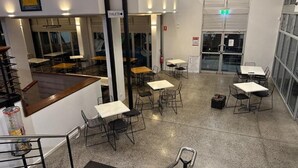 A hotel lobby with multiple tables and chairs, a staircase, and a sign indicating the location of toilets. - Eatons Hotel (Muswellbrook)