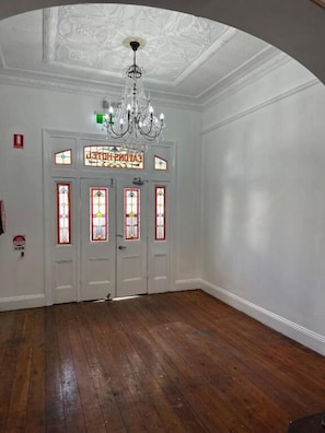 A room with a wooden floor, white walls, a chandelier, and stained glass doors. - Eatons Hotel (Muswellbrook)