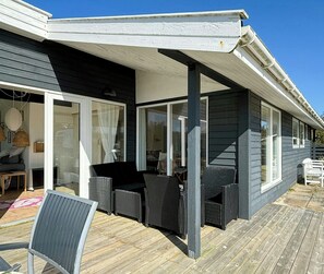 A covered outdoor seating area with wicker furniture and a wooden deck. - Idyllic holiday home charm in Nr. Lyngby (Løkken)