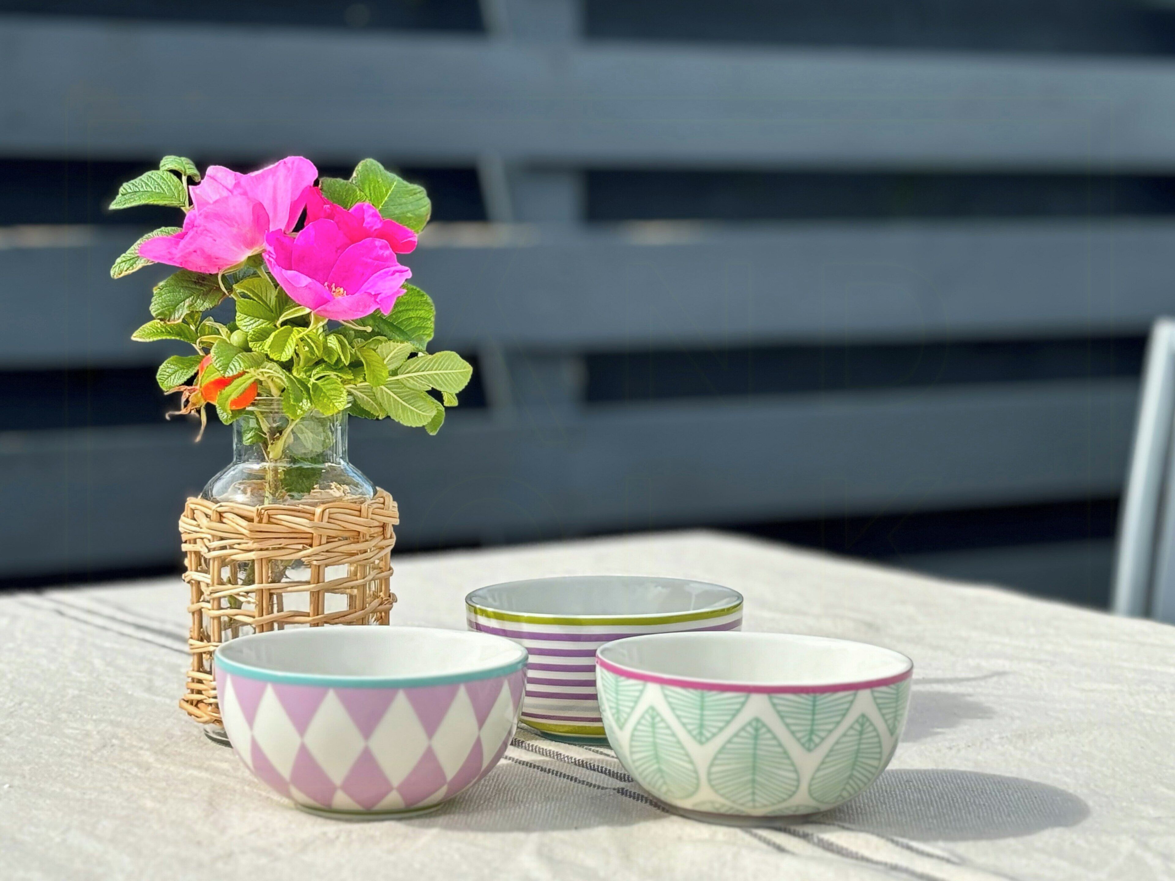 Een tafel met een rieten mand vol roze bloemen en twee decoratieve kommen.