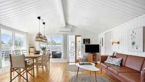 A spacious living area with a wooden floor, a brown leather sofa, a white table, and a dining set. - Idyllic holiday home charm in Nr. Lyngby (Løkken)